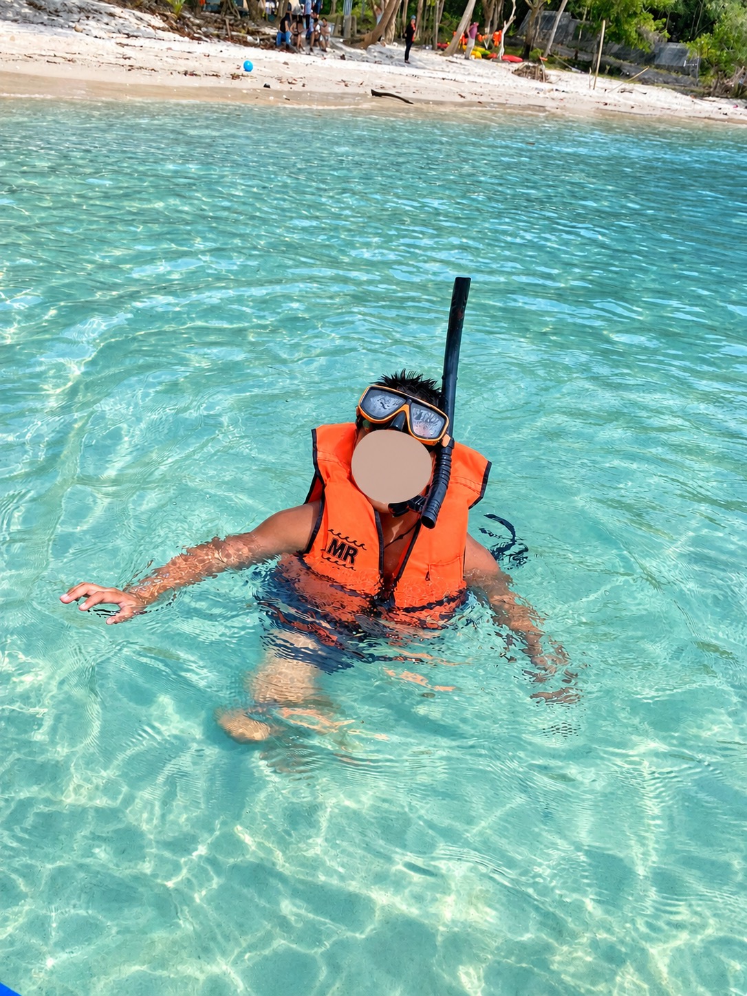 Child with snorkelling equipment and orange life jacket in the sea