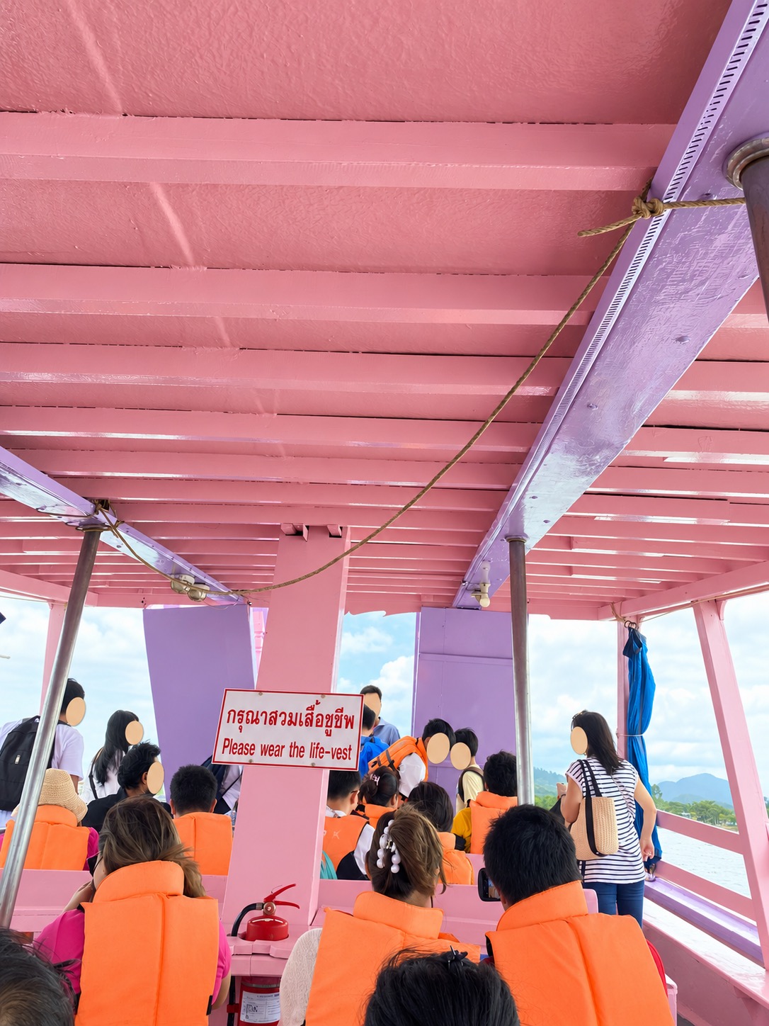 Passengers in orange life vests inside the pink ferry