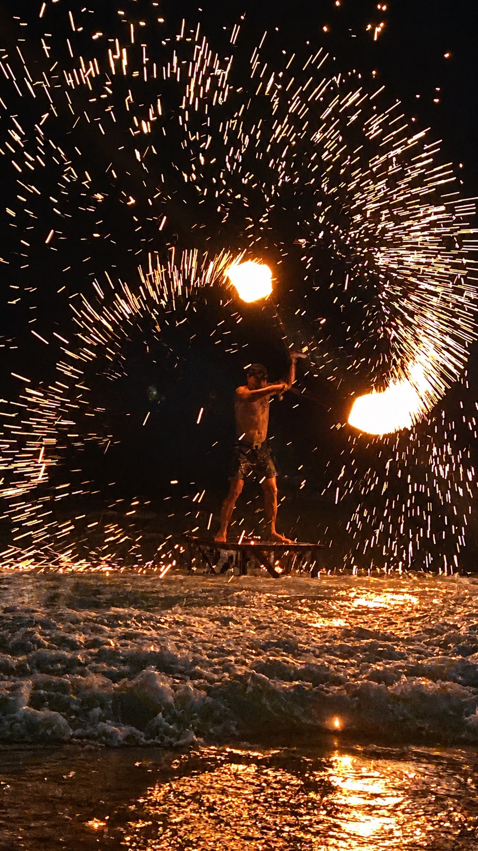 Fire dancer performing with sparks on the beach at night