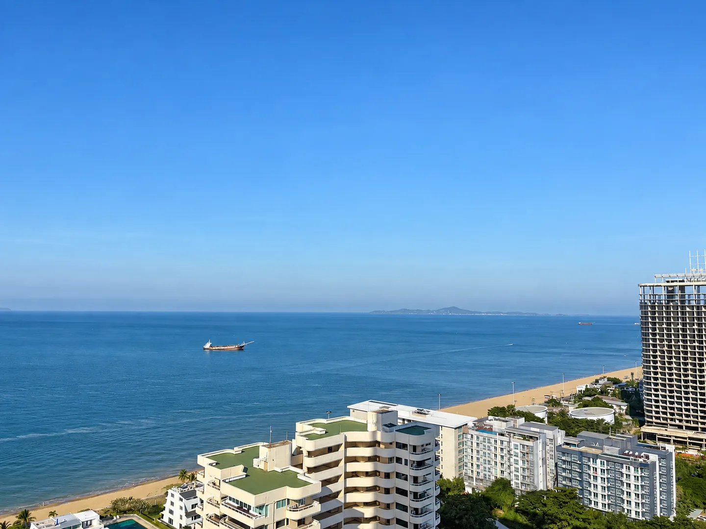 View from a Pattaya condo over beachfront buildings, the sandy shoreline and sea.