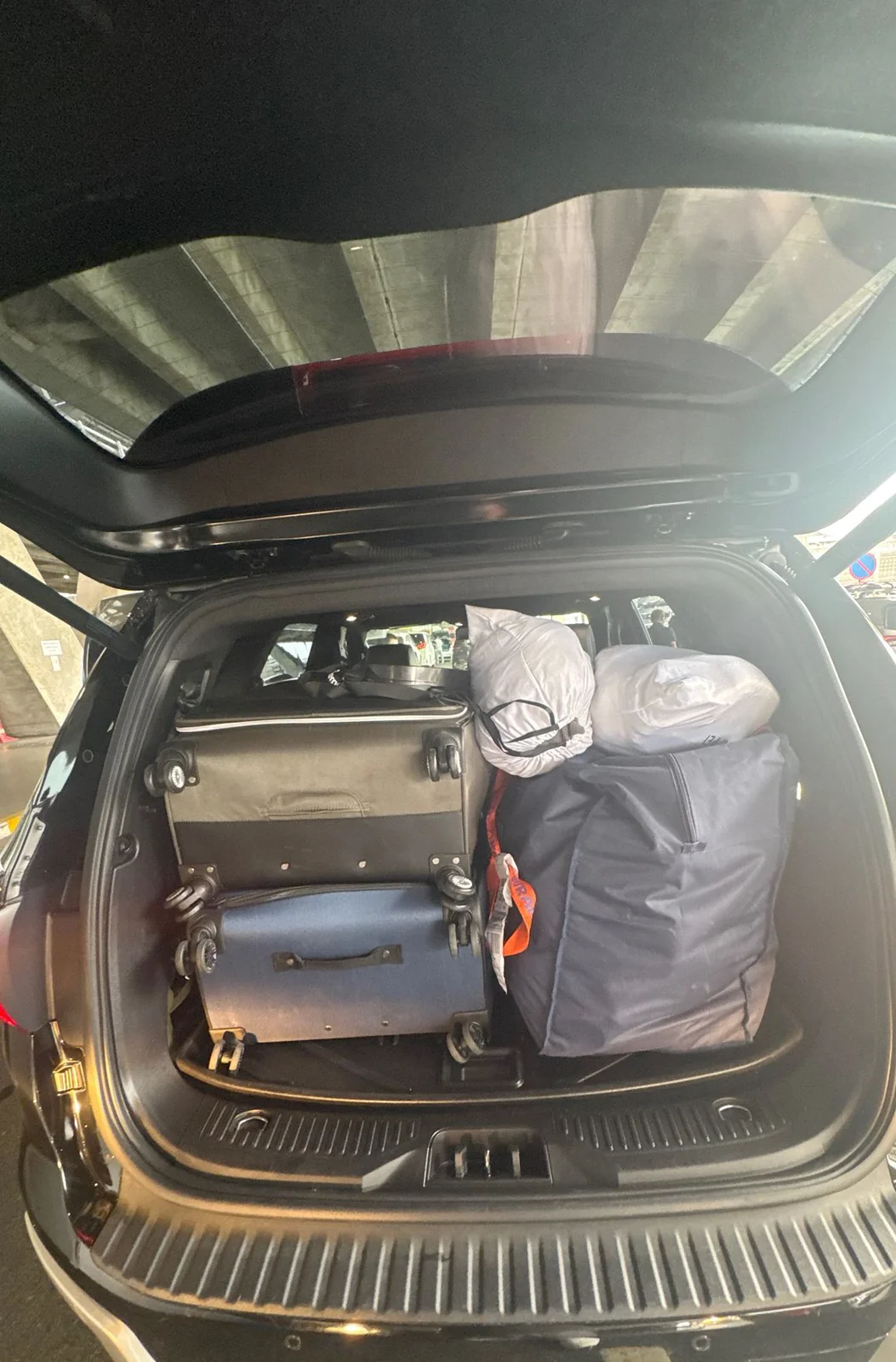 Open SUV boot packed with two wheeled suitcases and bulky travel bags.